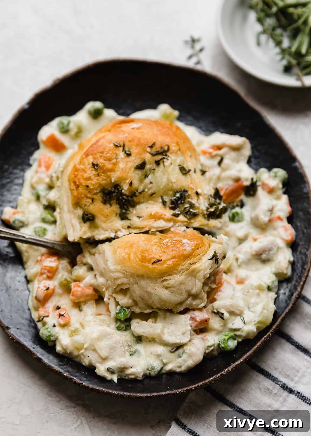 Golden-Crusted Skillet Chicken Pot Pie 8 A biscuit and chicken pot pie mixture on a black plate with a fork cutting into the biscuit.