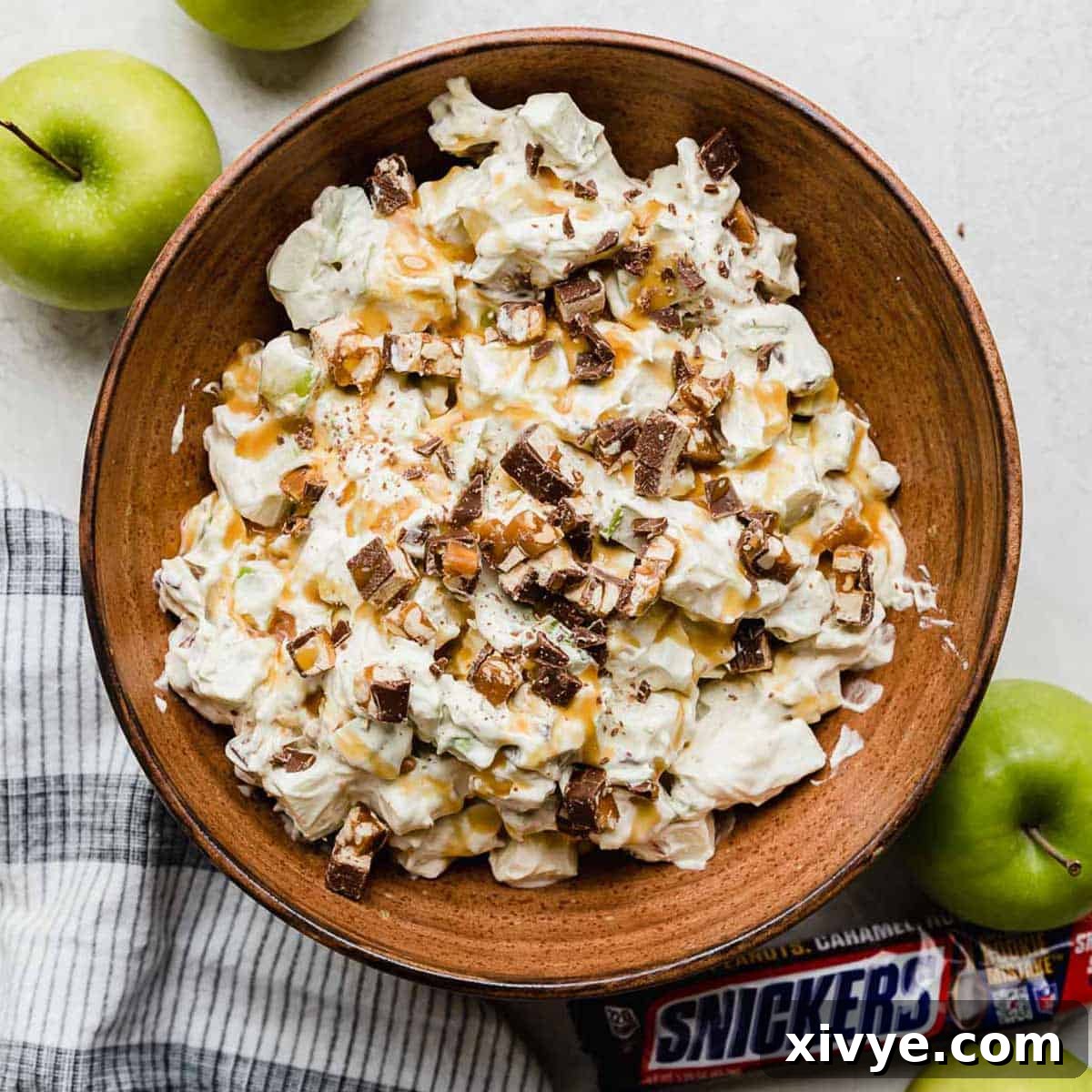 Snickers Apple Delight 7 Overhead photo of a salad with snickers and apples in a brown bowl topped with caramel to make the best Apple Snickers Salad recipe.