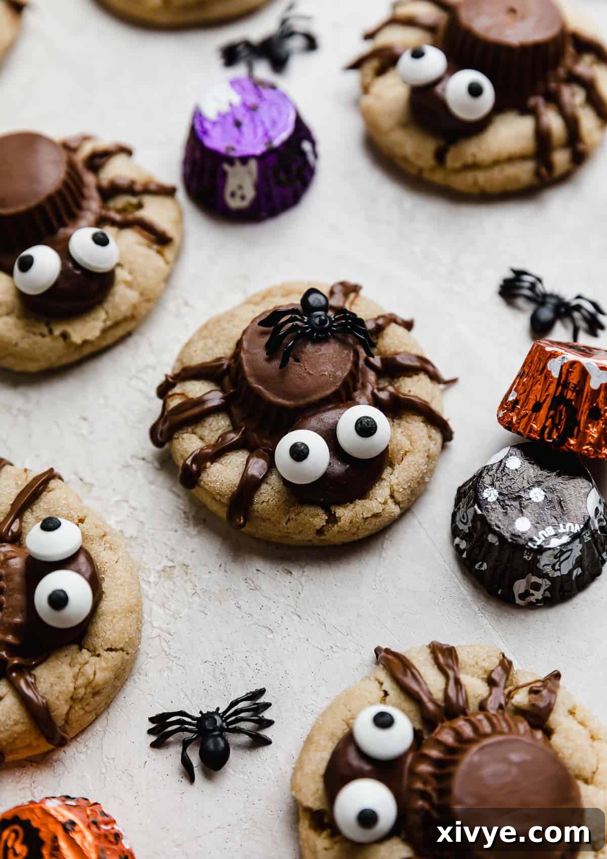 Delicious Halloween Spider Cookies featuring a peanut butter cookie base, an upside-down Reese's peanut butter cup body, a Milk Dud head, and expressive candy eyes, all decorated with eight piped chocolate legs.