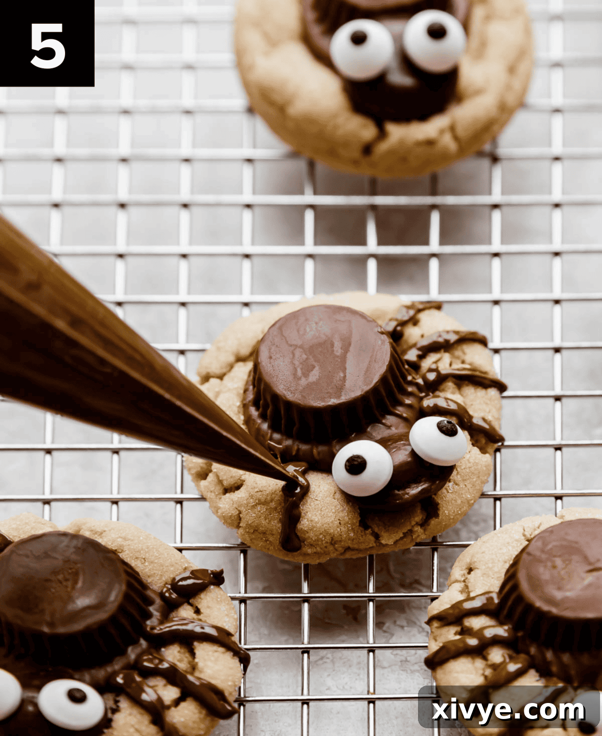 A Halloween peanut butter spider cookie being decorated with melted chocolate piped into eight spider legs, showcasing the delicate piping process.