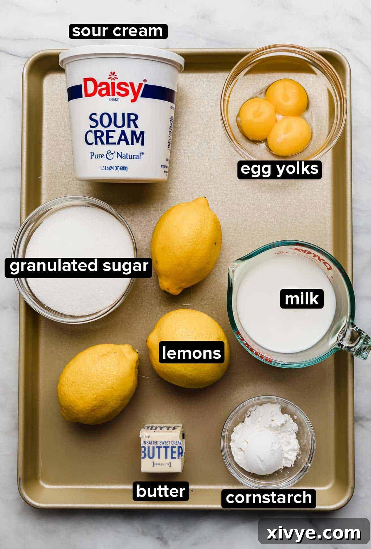 Tangy Lemon Dream Pie 3 Lemon Sour Cream Pie ingredients on a gold baking sheet: sour cream, egg yolks, sugar, lemons, cornstarch, butter, and milk.