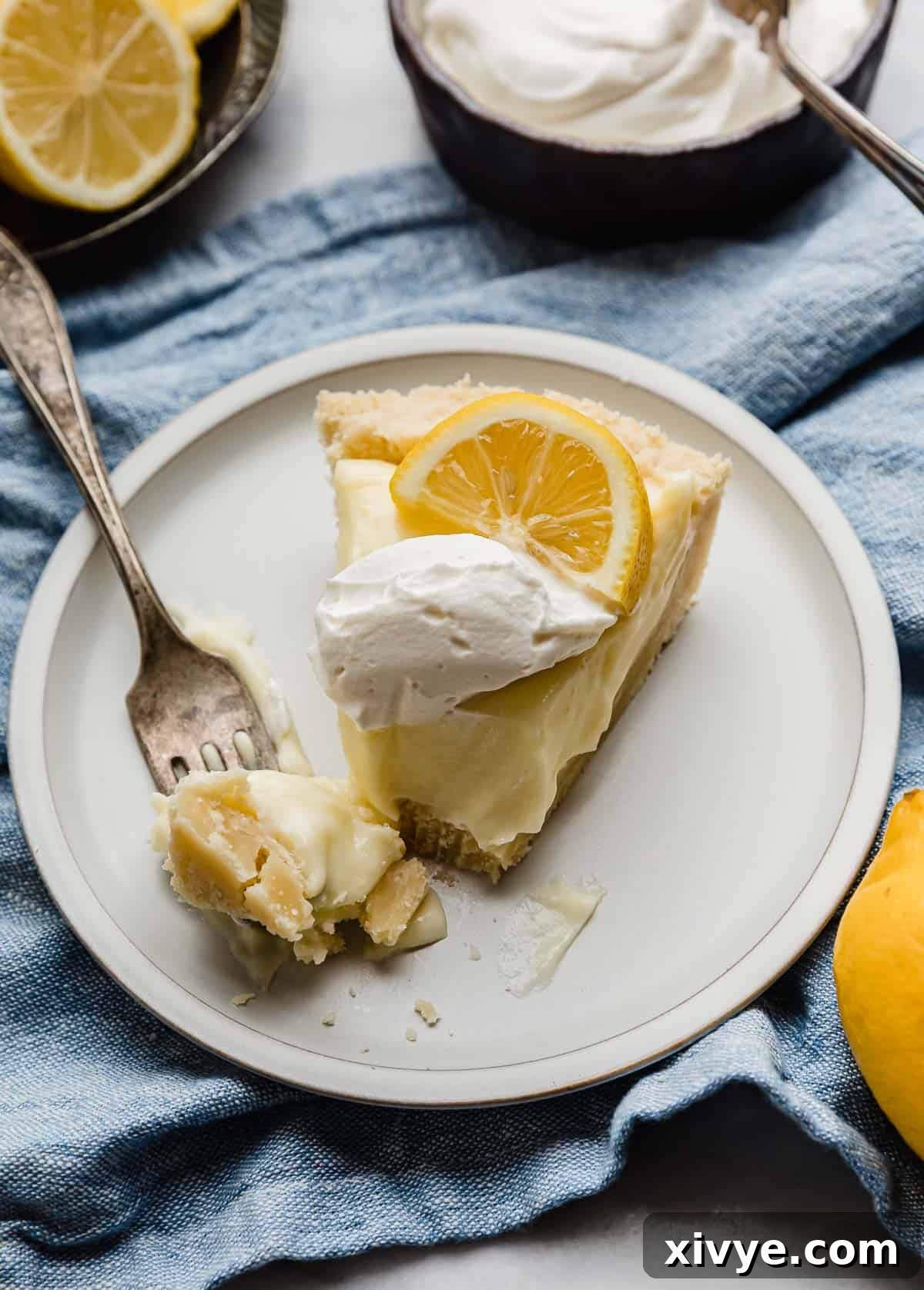 Tangy Lemon Dream Pie 7 Slice of the best Lemon Sour Cream Pie on a white plate, with a fork cutting into the tip of the pie.