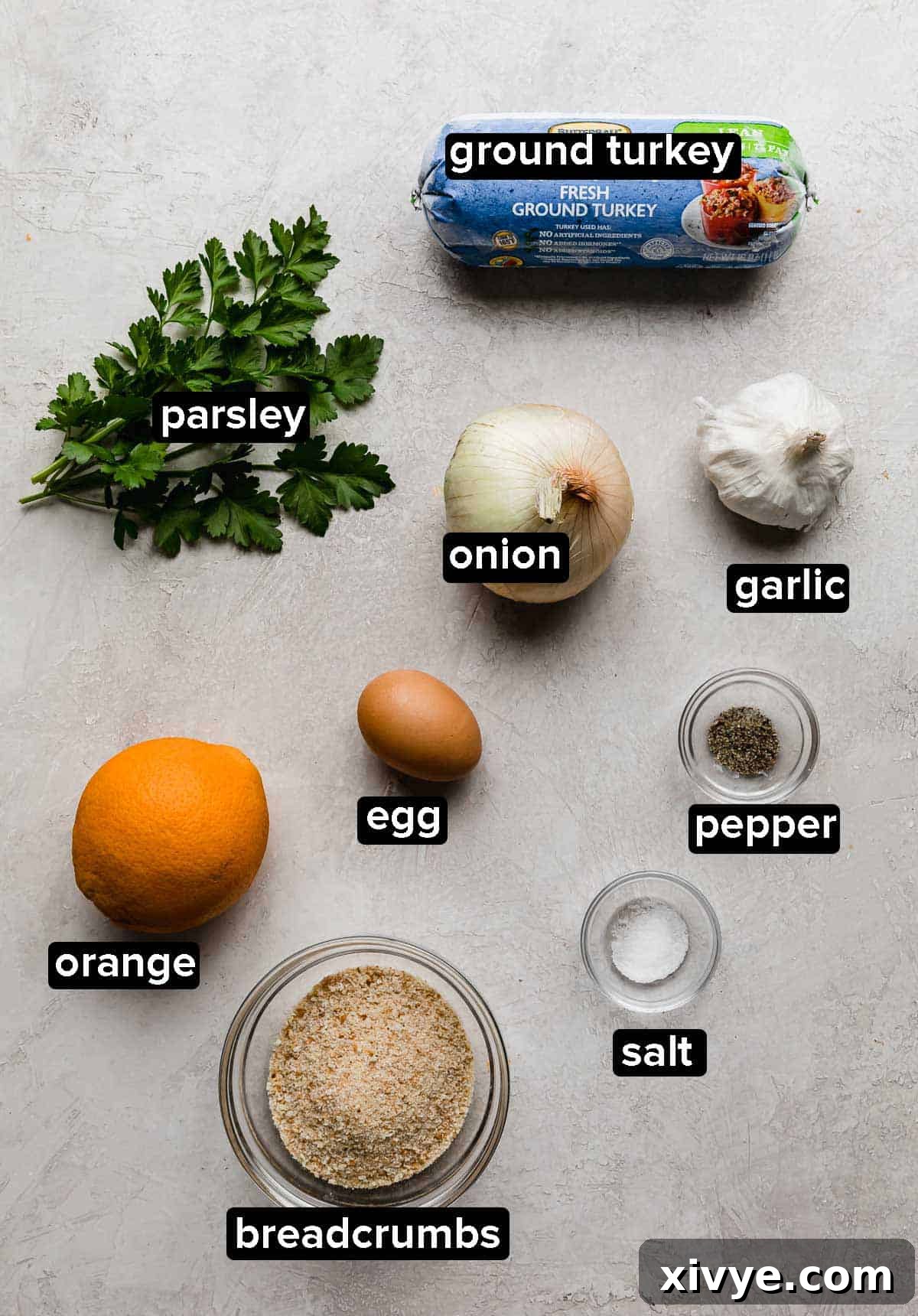 Christmas turkey meatballs ingredients on a light gray background, which include: parsley, orange, breadcrumbs, egg, onion, and turkey.