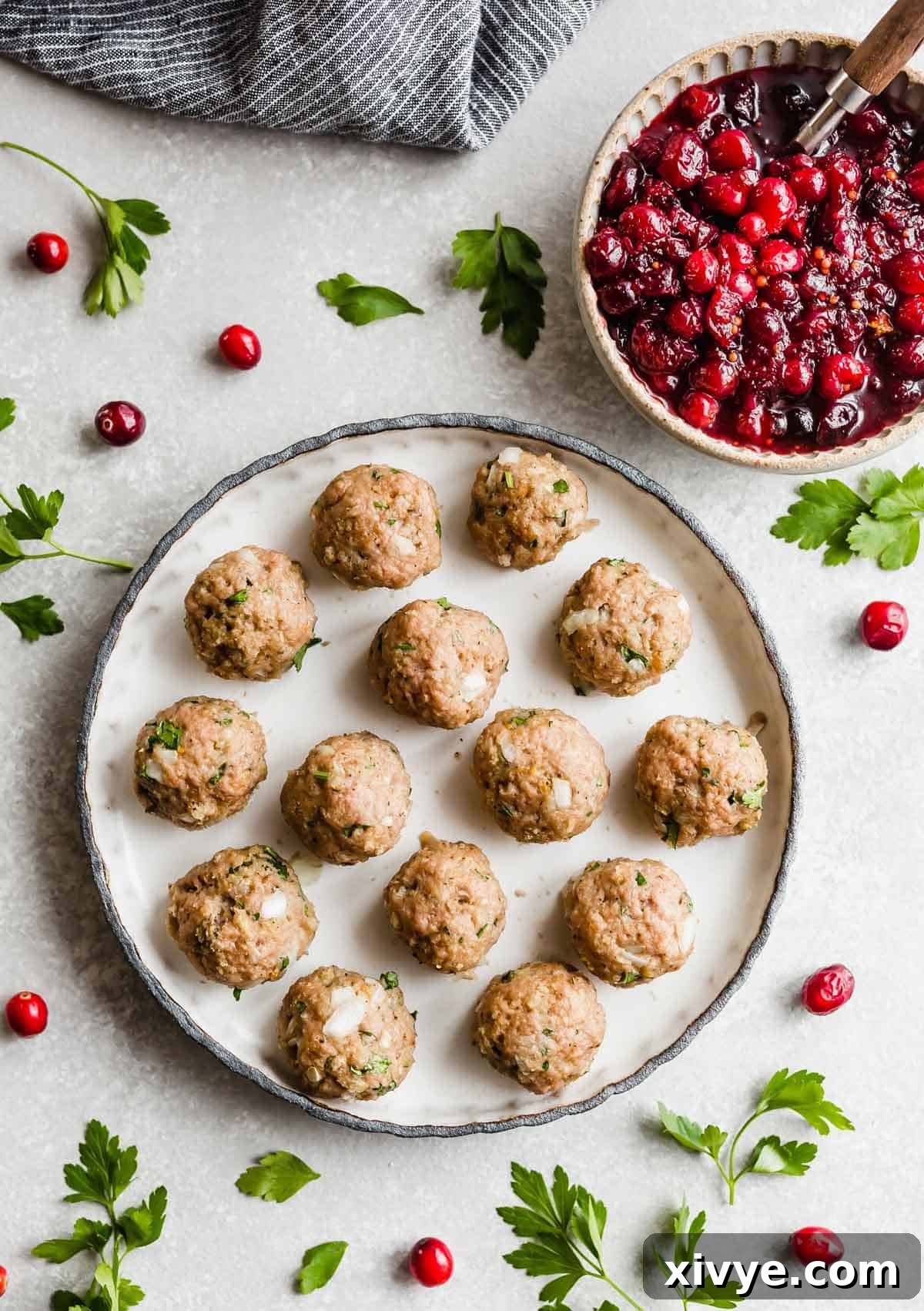 A black rimmed white plate filled with baked turkey meatballs with cranberry chutney in a small bowl to the top right of the plate.