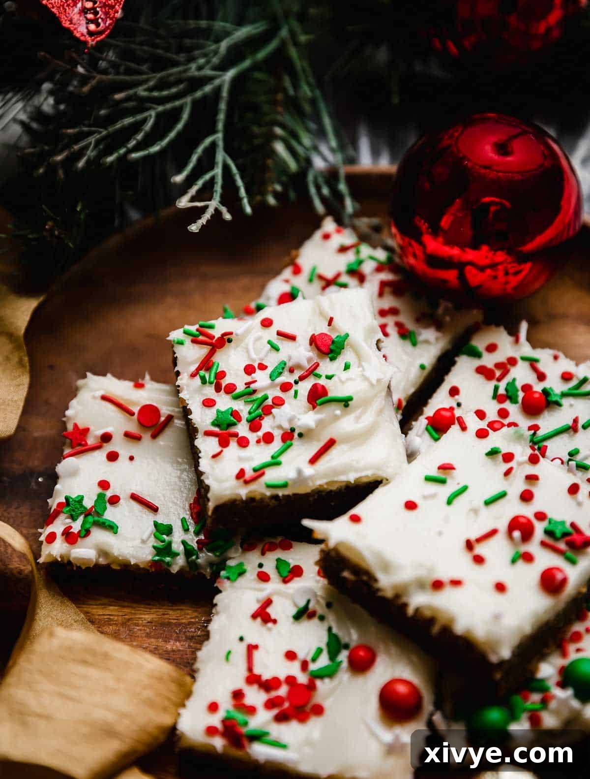 Warm Spiced Ginger Bars 2 Gingerbread Cookie Bars topped with cream cheese frosting and red and green sprinkles, on a brown plate.