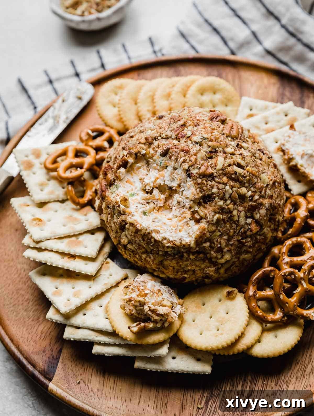 A Christmas Cheese Ball covered with pecans on a brown plate surrounded by crackers.
