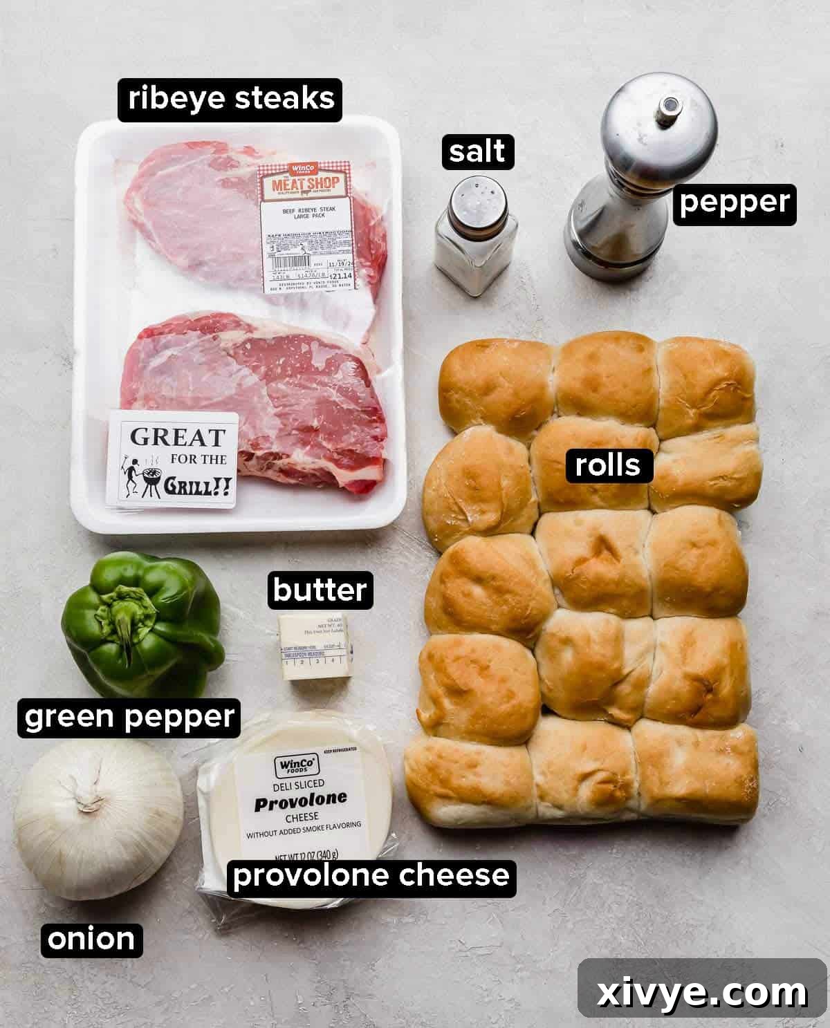 Ultimate Philly Cheesesteak Sliders 3 Philly Cheesesteak Sliders ingredients on a gray background: ribeye steaks, rolls, onion, green pepper, provolone cheese, butter, rolls, and salt and pepper.