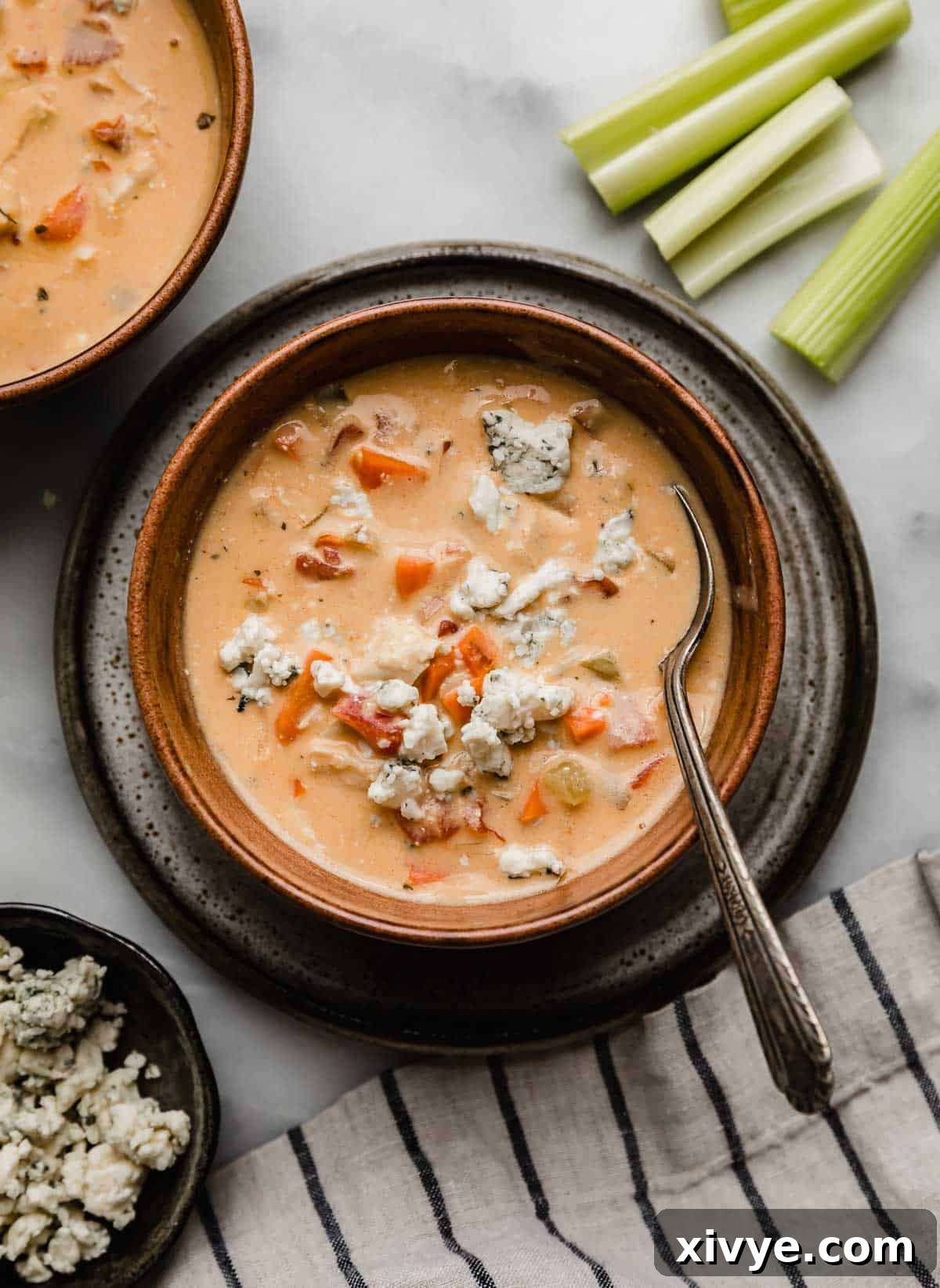 Overhead photo of Buffalo Chicken Soup topped with blue cheese in a brown bowl on a marble white background.