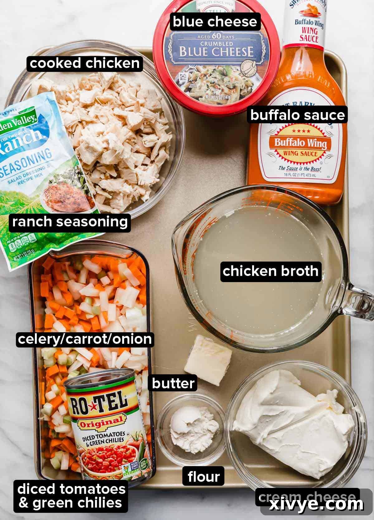 Buffalo Chicken Soup ingredients on a gold baking sheet: chicken, buffalo sauce, onions/carrots/celery, flour, cream cheese, and ranch seasoning.