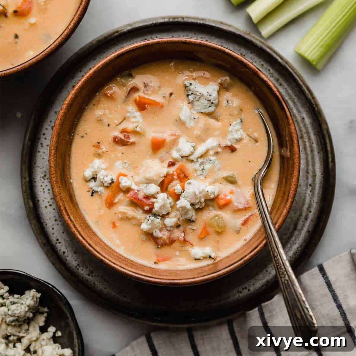 Buffalo chicken soup recipe in a brown bowl that's on a gray plate with blue cheese crumbles overtop of the soup.
