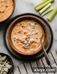 Overhead photo of Buffalo Chicken Soup topped with blue cheese in a brown bowl on a marble white background.