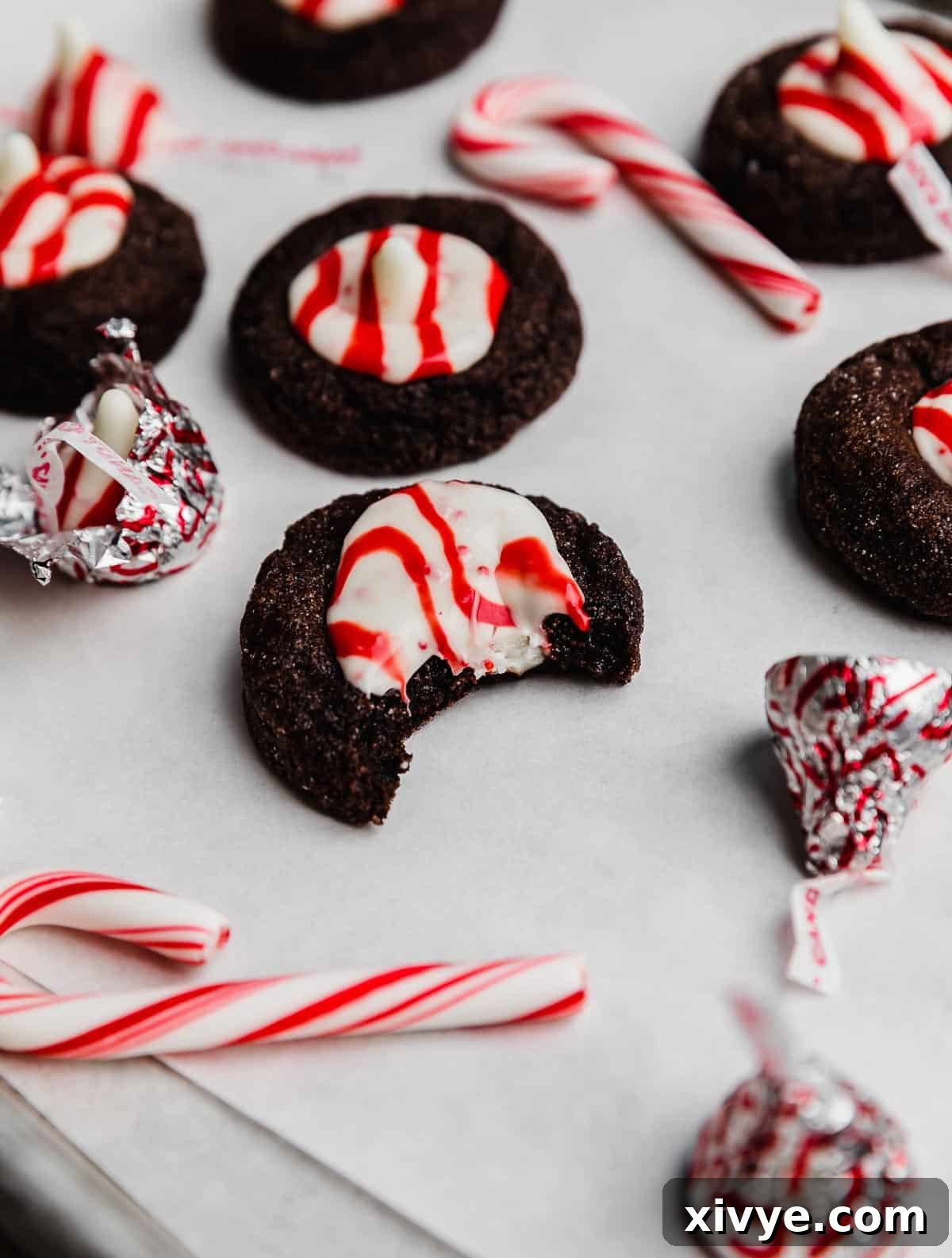 A chocolate peppermint blossom cookie on a white parchment paper with a bite taken out of the cookie.