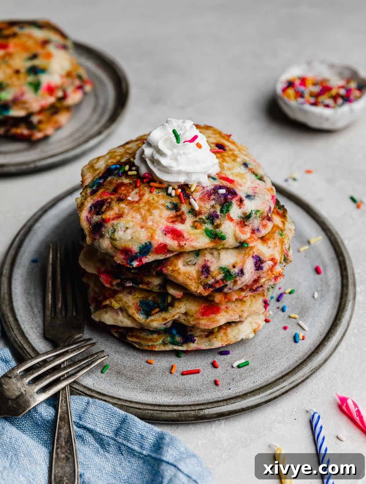 Birthday Cake Pancakes on a gray plate on a light gray background with birthday candles next to the plate.
