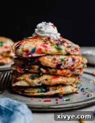 A stack of Birthday Cake Pancakes with whipped cream on top against a black background.