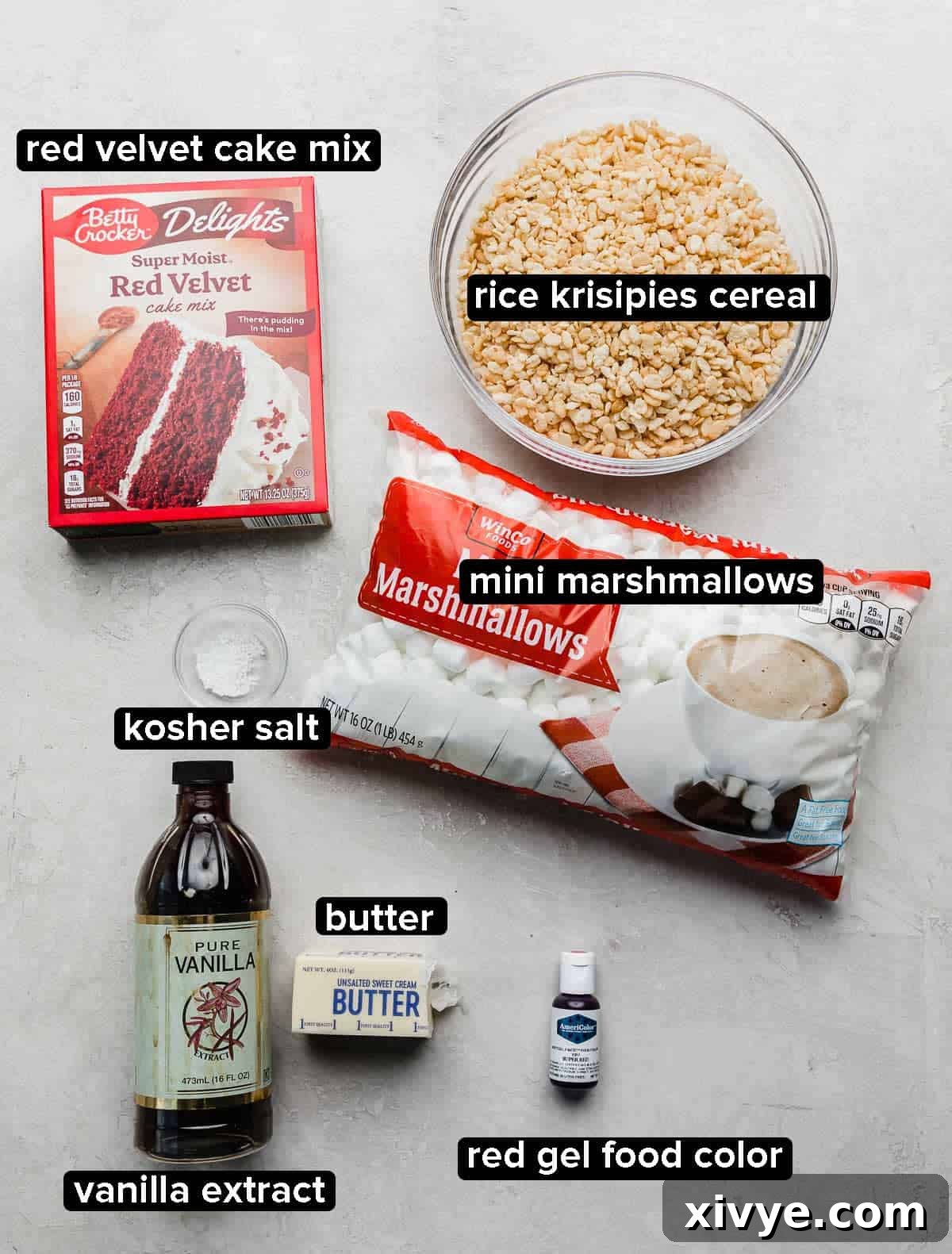 Red Velvet Rice Krispies ingredients on a light gray background: mini marshmallows, Rice Krispies cereal, vanilla, butter, red velvet box cake mix, and red food color.
