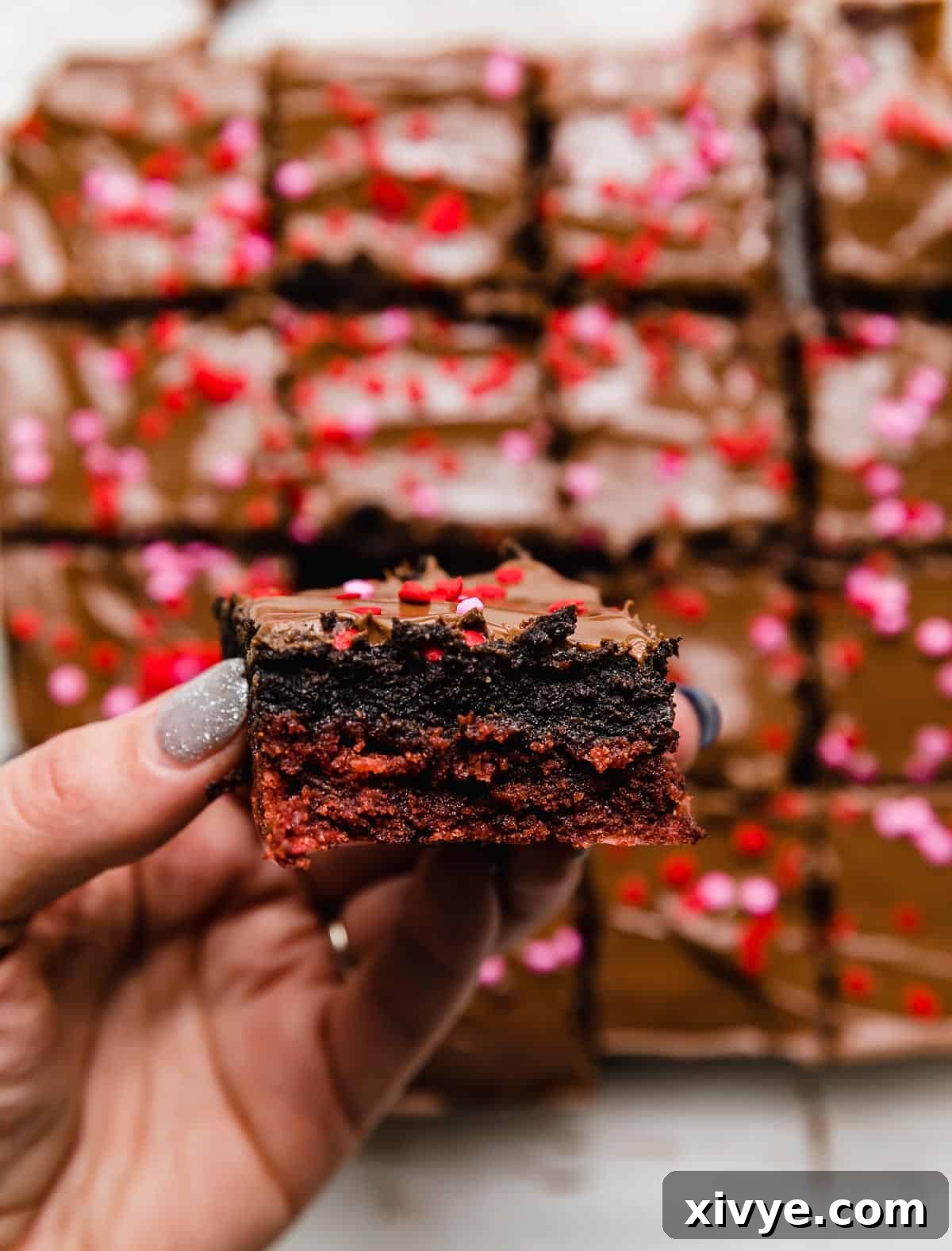 Decadent Red Velvet Oreo Truffle Brownies 8 A hand holding a Valentines brownie, featuring a red velvet base, Oreo truffle center, and melted milk chocolate overtop.