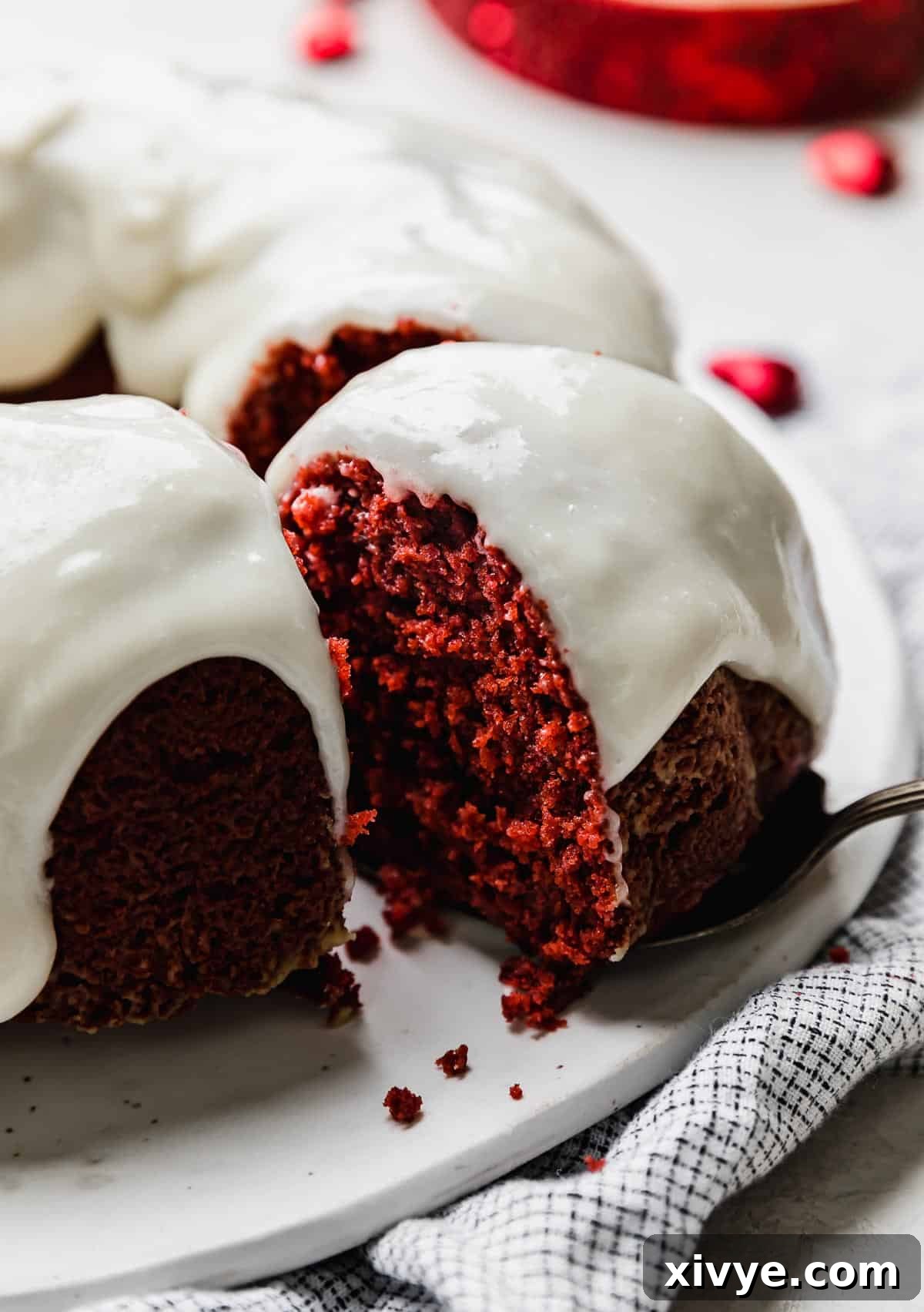 Crimson Crown Bundt 2 A moist Red Velvet Bundt Cake topped with cream cheese glaze and a slice of cake partially removed from the red bundt cake.