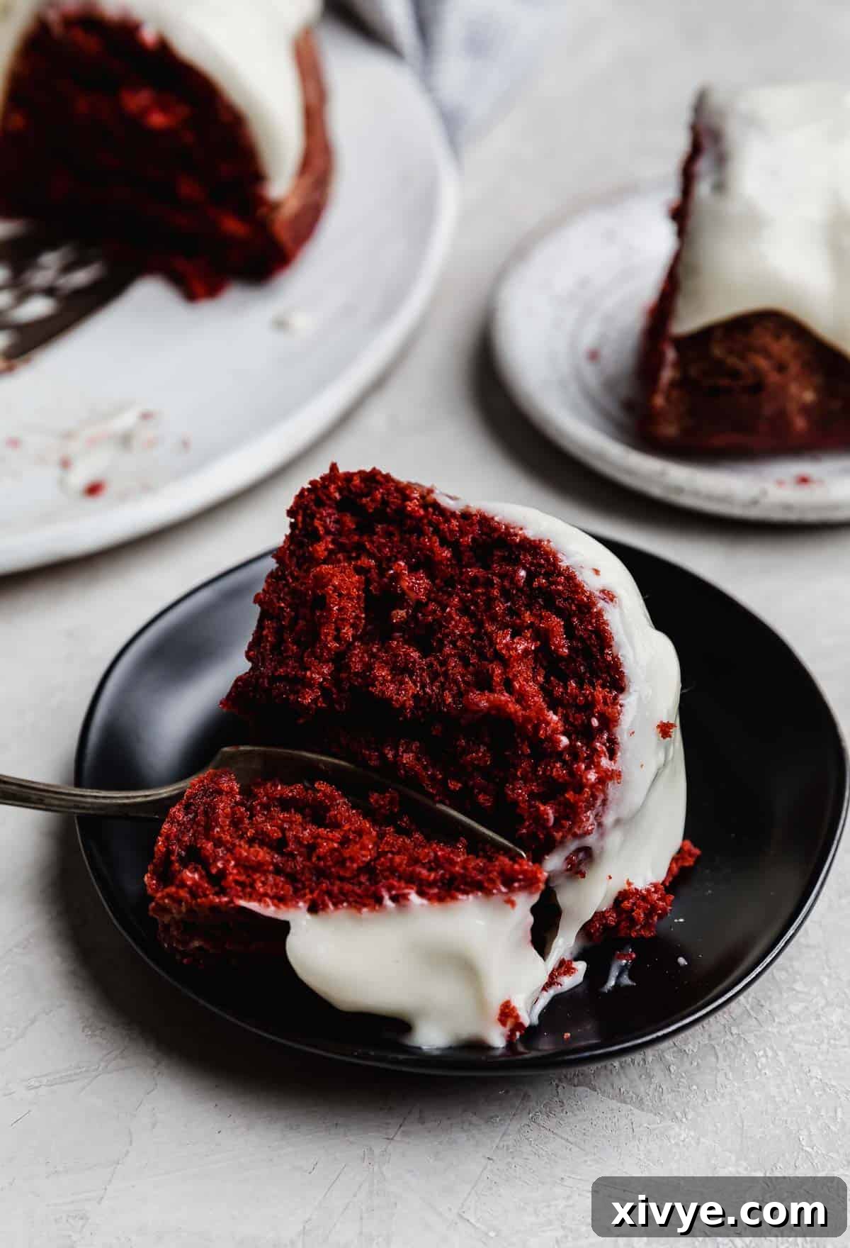 Crimson Crown Bundt 9 A slice of Red Velvet Bundt Cake topped with glaze on a black plate.