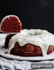 Crimson Crown Bundt 10 A slice of red valentines day bundt cake hovering over a cream cheese glaze topped Red Velvet Bundt Cake against a black background.