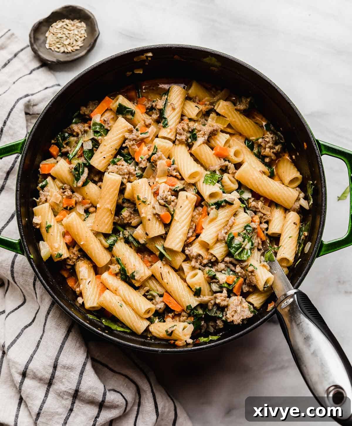 Hearty Italian Sausage Rigatoni 2 A green dutch oven filled with Italian Sausage Rigatoni with spinach on a white marble surface.