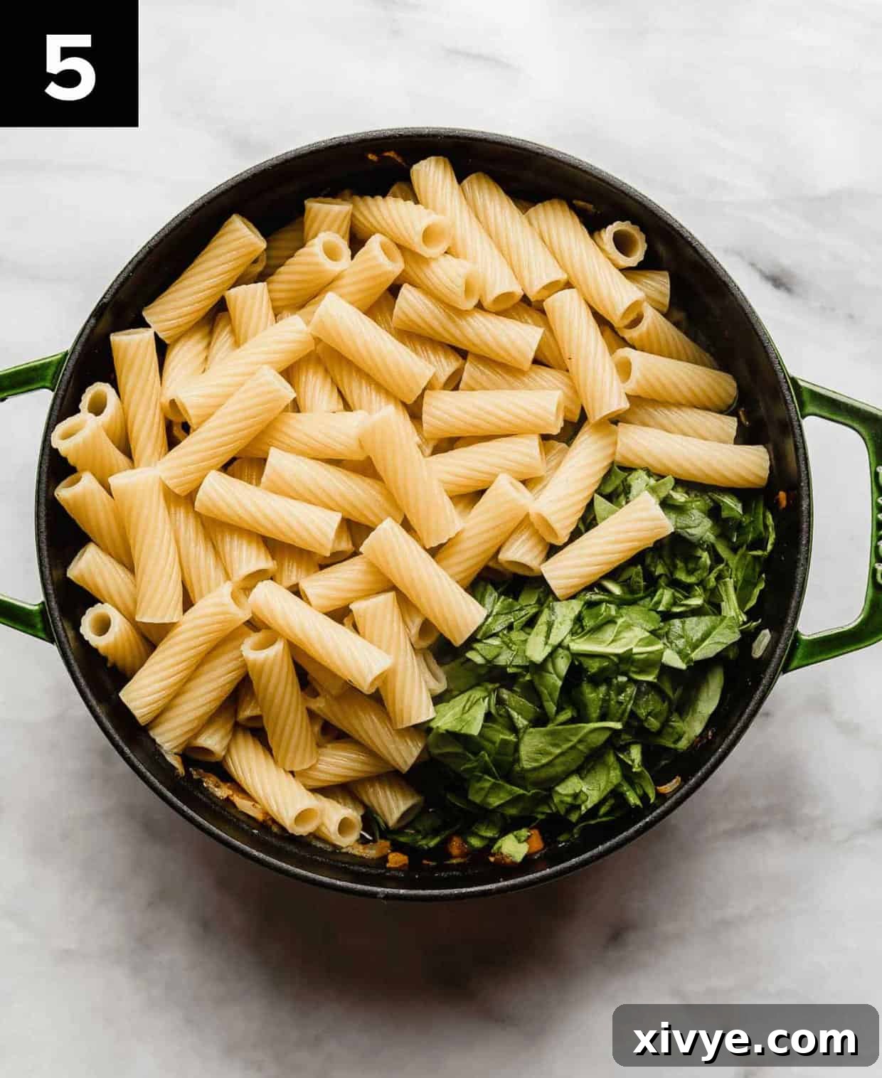 Hearty Italian Sausage Rigatoni 5 Cooked rigatoni noodles and chopped spinach in a large dutch oven on a white surface.