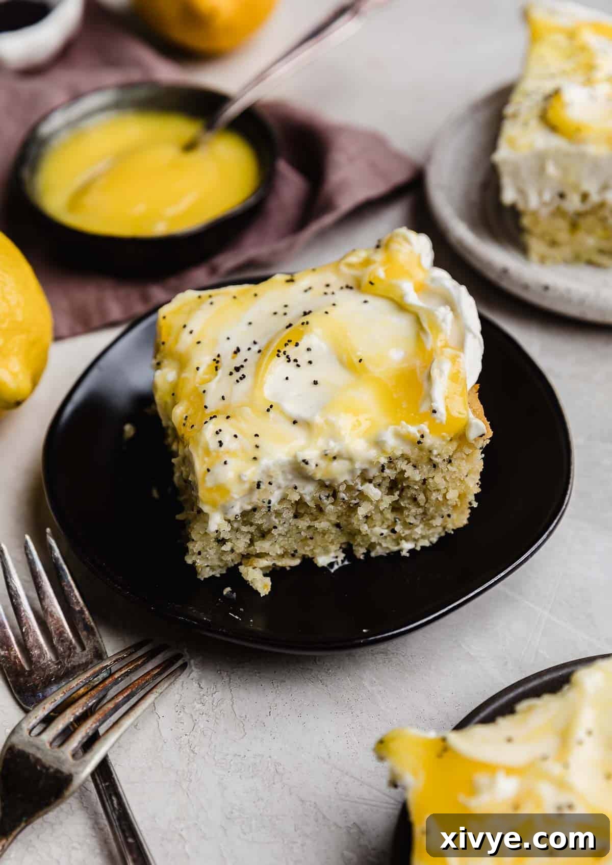 A lemon poppy seed sheet cake cut into a square on a black plate.