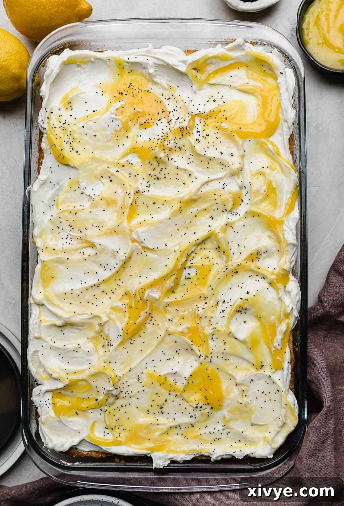 Overhead photo of lemon poppy seed cake topped with a whipped cream cheese frosting and dollops of homemade lemon curd on top.