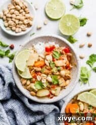 A bowl of Massaman Curry on a white background with a bowl of peanuts, and sliced limes next to it.