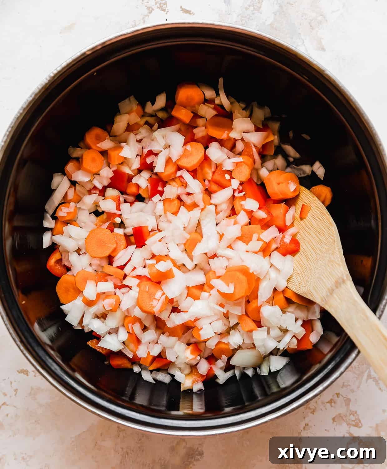 Black pot with chopped onion, red pepper, and carrots in it.