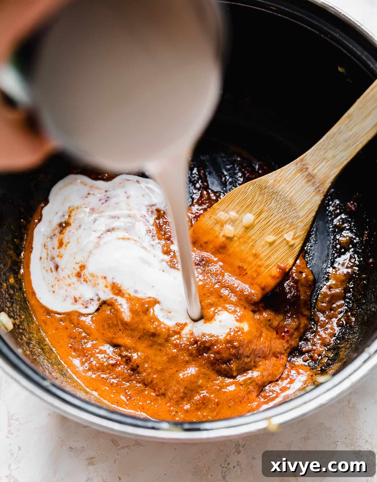 Coconut milk being poured into a pot with Massaman Curry paste at the bottom.