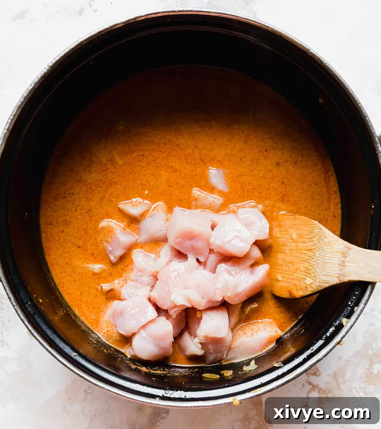 Raw, cubed chicken in a pot with massaman curry.