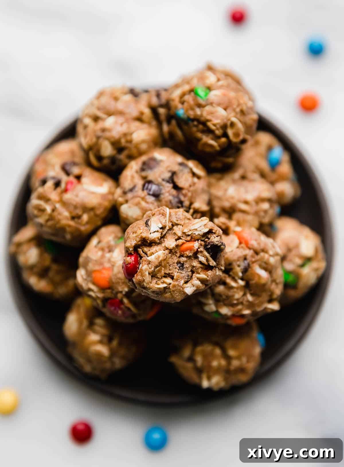 An inviting overhead photo showcasing Monster Cookie Protein Balls arranged on a sleek black plate, positioned on a clean white surface, highlighting their colorful appeal and perfectly round shape.