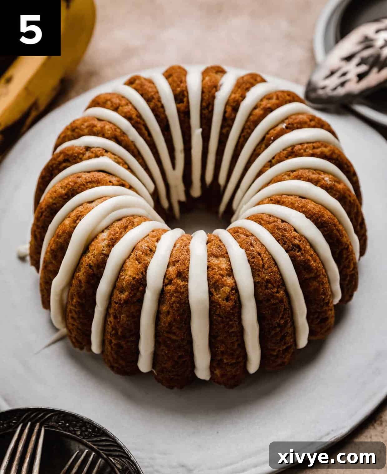 Golden Banana Bundt Delight 5 A cream cheese glazed Banana Bread Bundt Cake on a white cake plate.