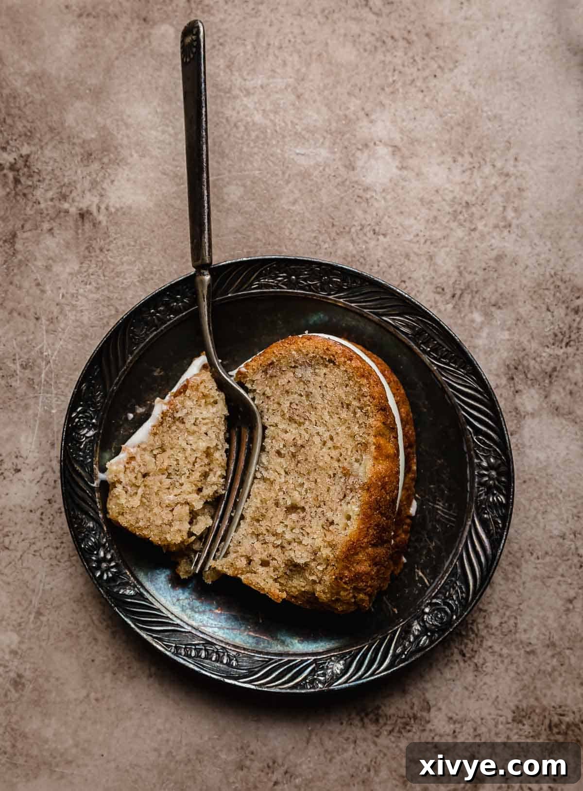 Golden Banana Bundt Delight 6 A slice of Banana Bread Bundt Cake on a black antique plate with a fork cutting into the bundt cake.