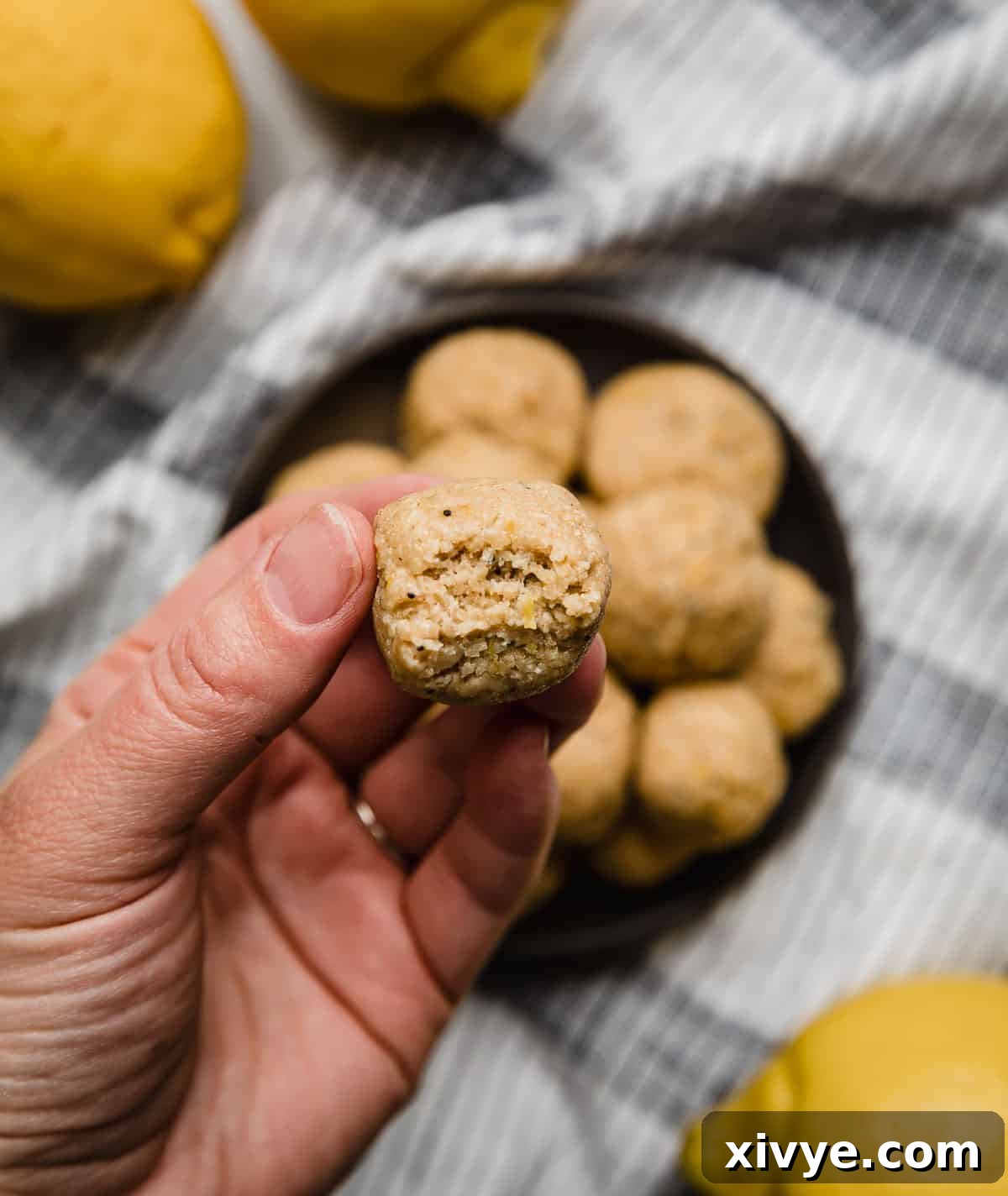 A hand holding a Lemon Protein Bite with a bite taken out of the protein ball.