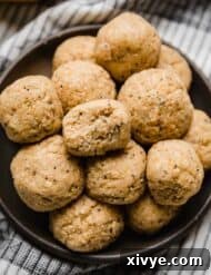 A bite taken out of a Lemon Protein Ball that's stacked on a black plate with other lemon poppy seed protein balls.