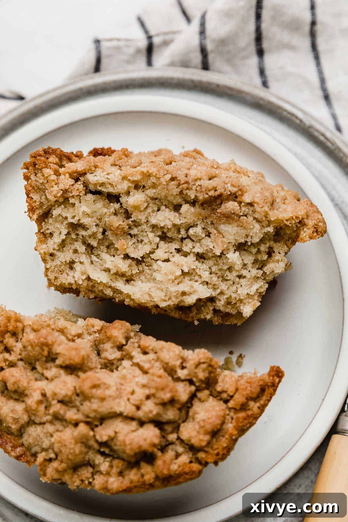 Close up photo of a Banana Bread Crumb Muffin cut in half on a white plate.
