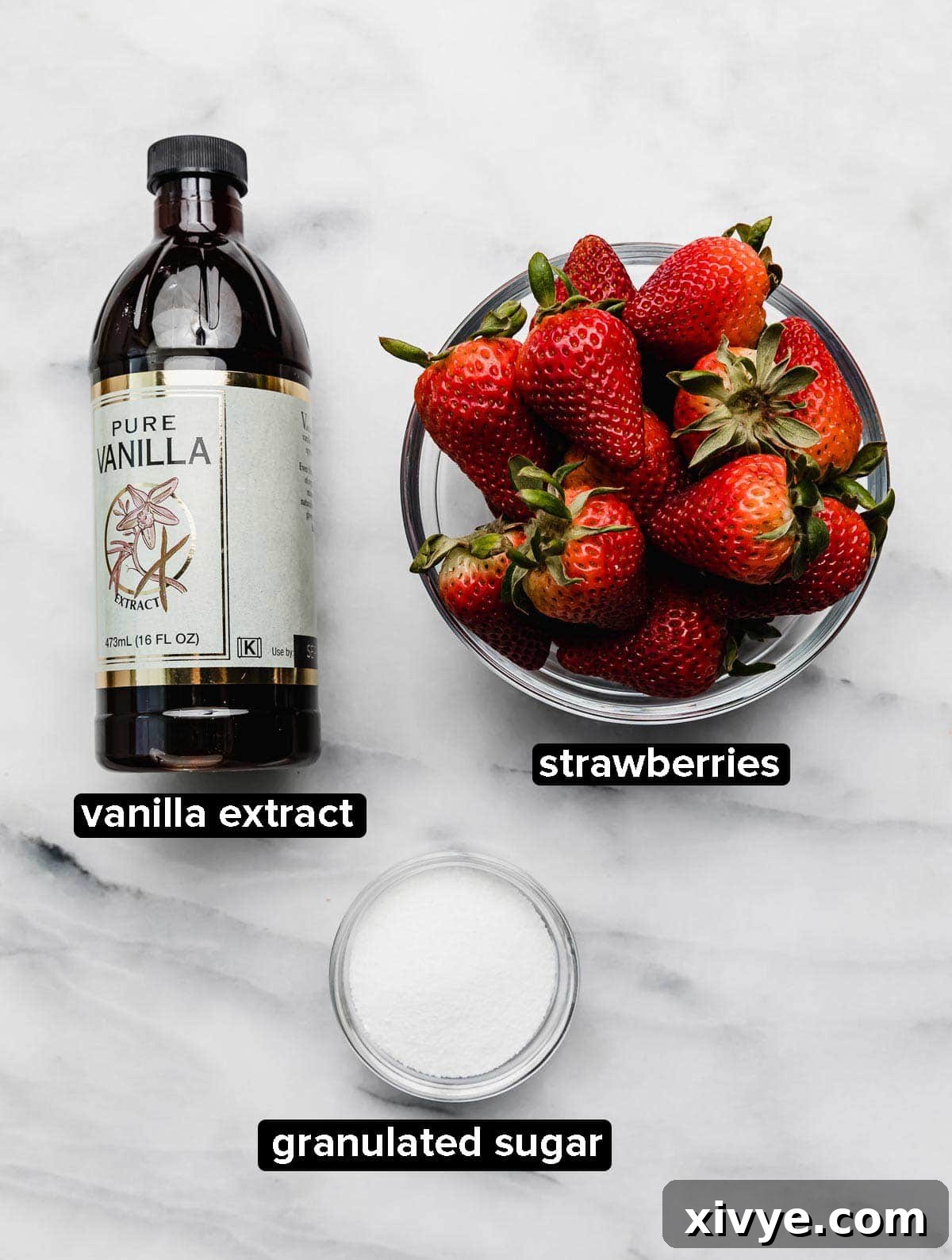 Ingredients used to roast strawberries in the oven: vanilla, fresh strawberries, and granulated sugar on a white surface.