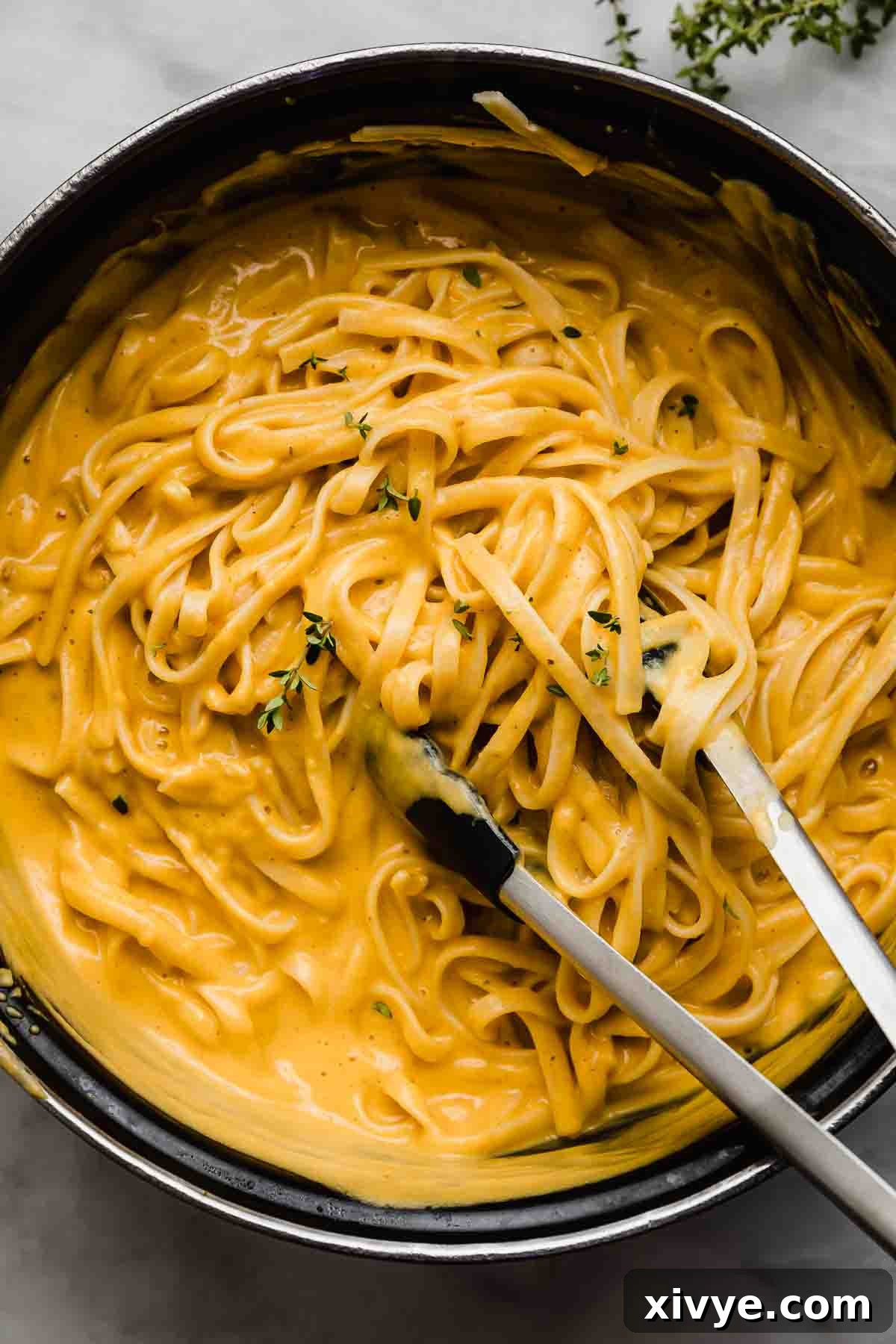 Velvety Butternut Alfredo 2 Creamy Butternut Squash Alfredo in a black pot with kitchen tongs mixing the noodles.