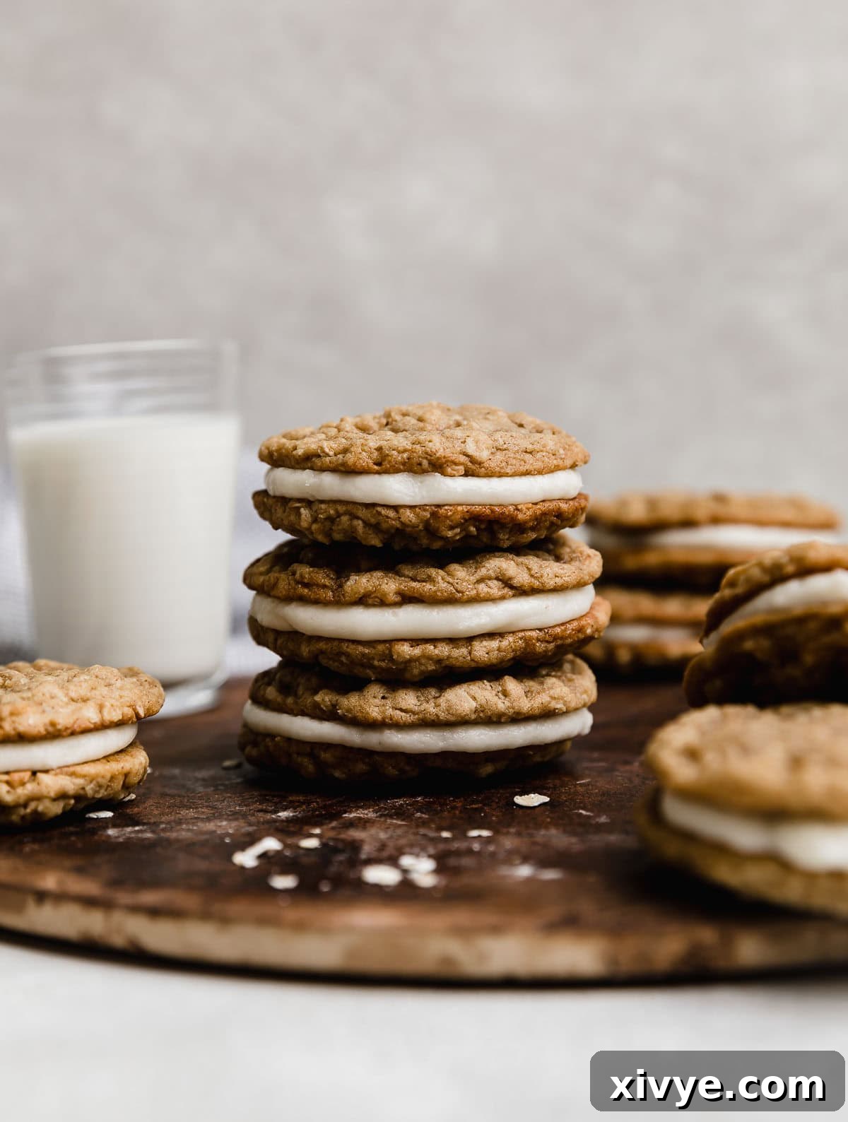 Three homemade oatmeal creme pies stacked on top of each other with a glass of milk in the background, showcasing their soft texture and creamy filling.