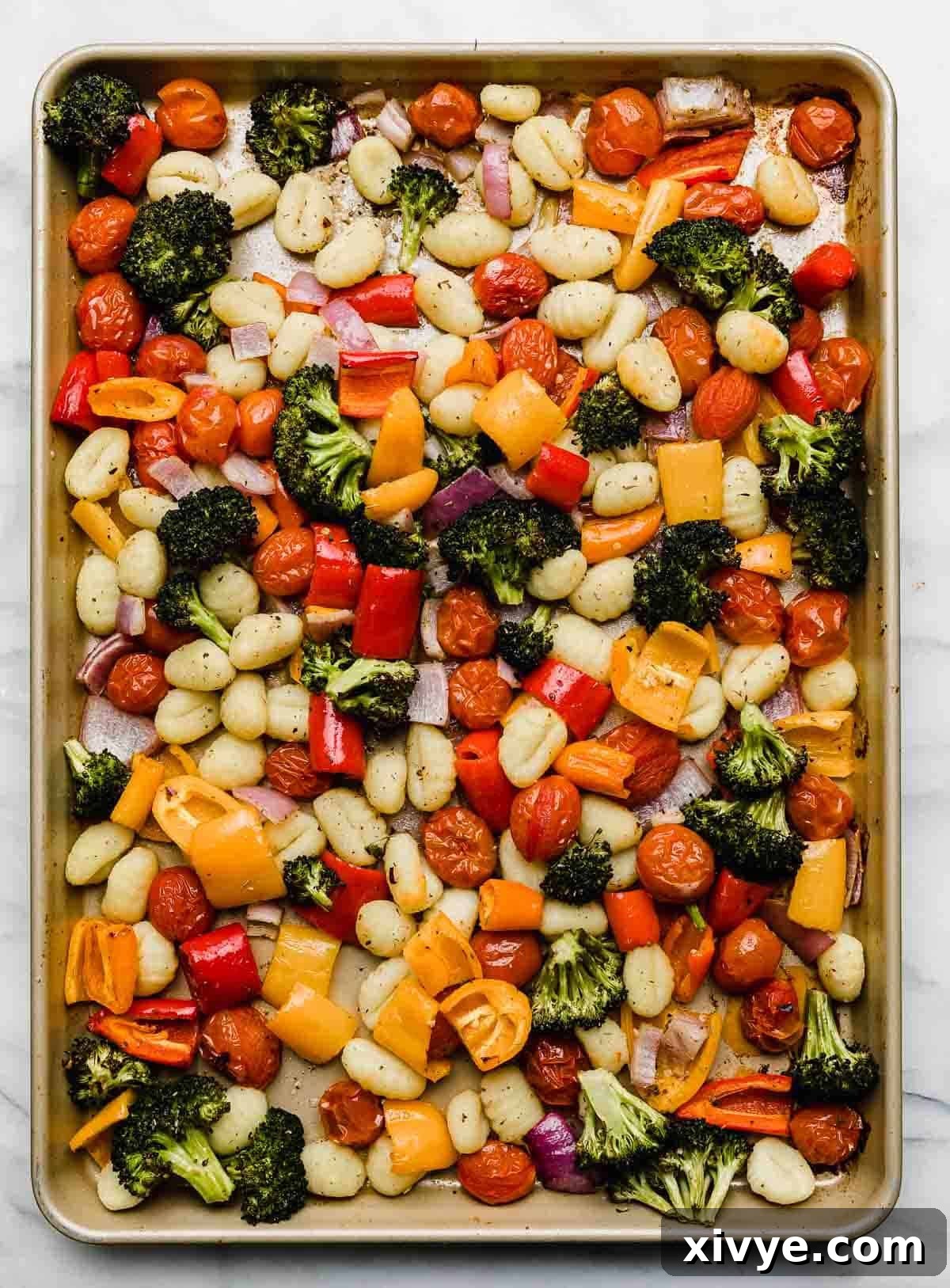 A vibrant sheet pan filled with golden-brown gnocchi and an array of roasted vegetables including bright green broccoli florets, colorful bell peppers, juicy red grape tomatoes, and thinly sliced red onion.