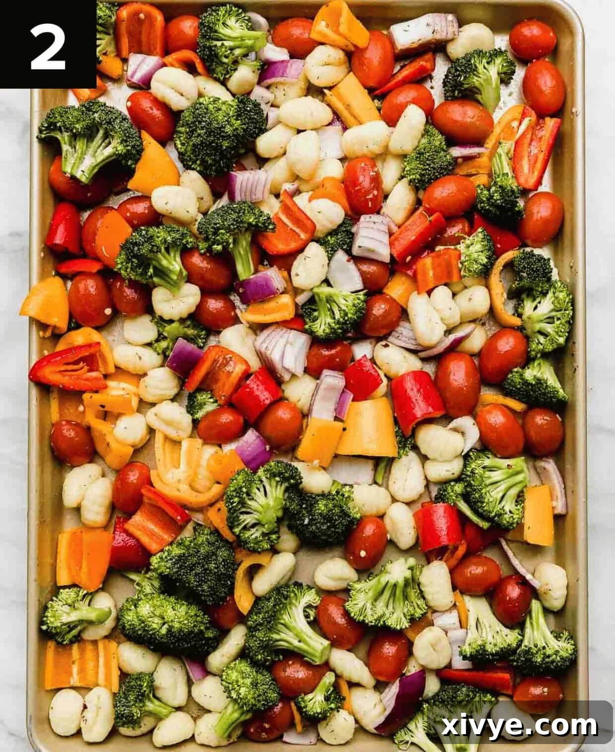 Close-up of colorful vegetables and gnocchi tossed together on a baking sheet, glistening with olive oil and spices, ready for roasting.