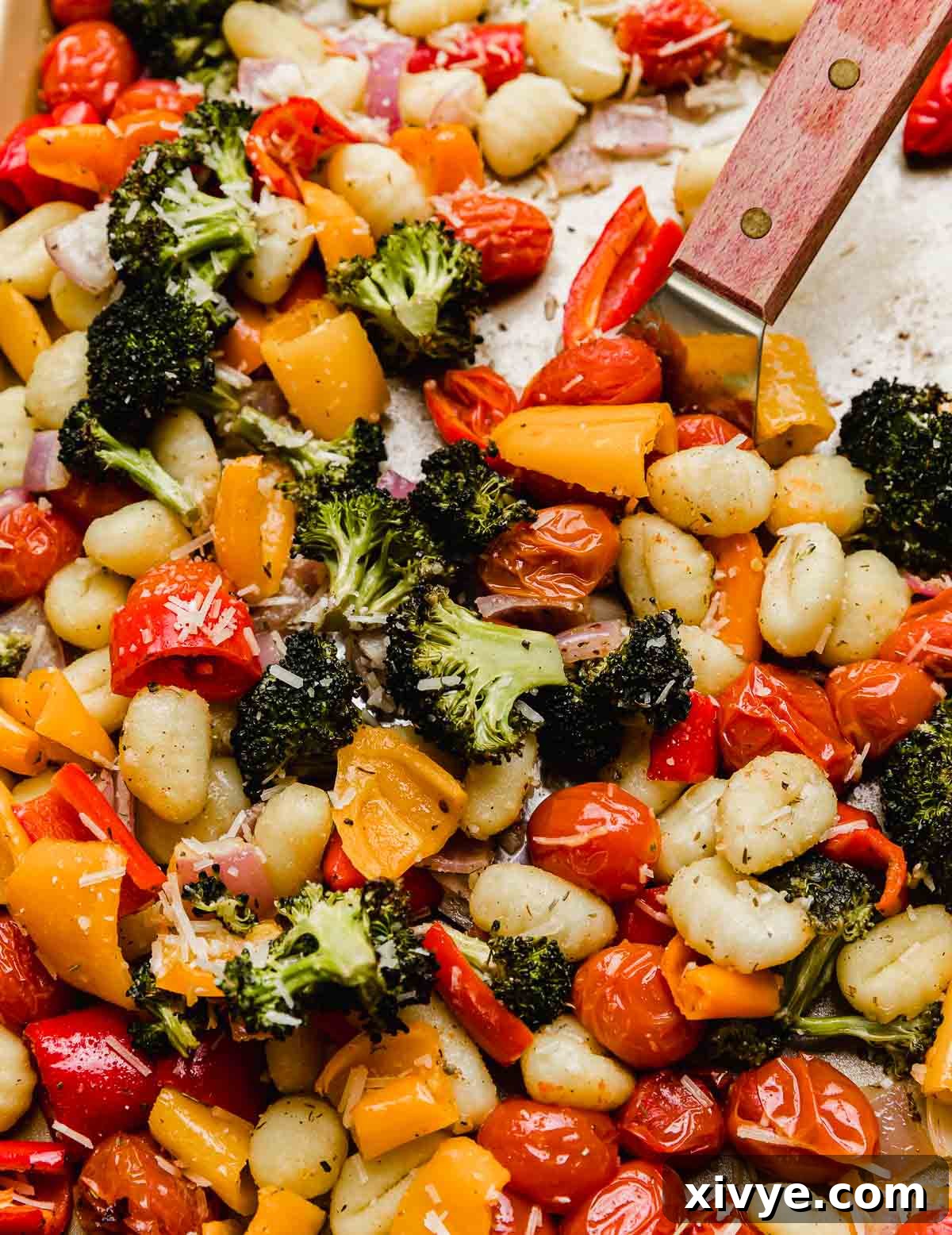 A metal spatula lifting a portion of roasted gnocchi and vegetables from a baking sheet, showcasing the crispy gnocchi and tender, caramelized vegetables.