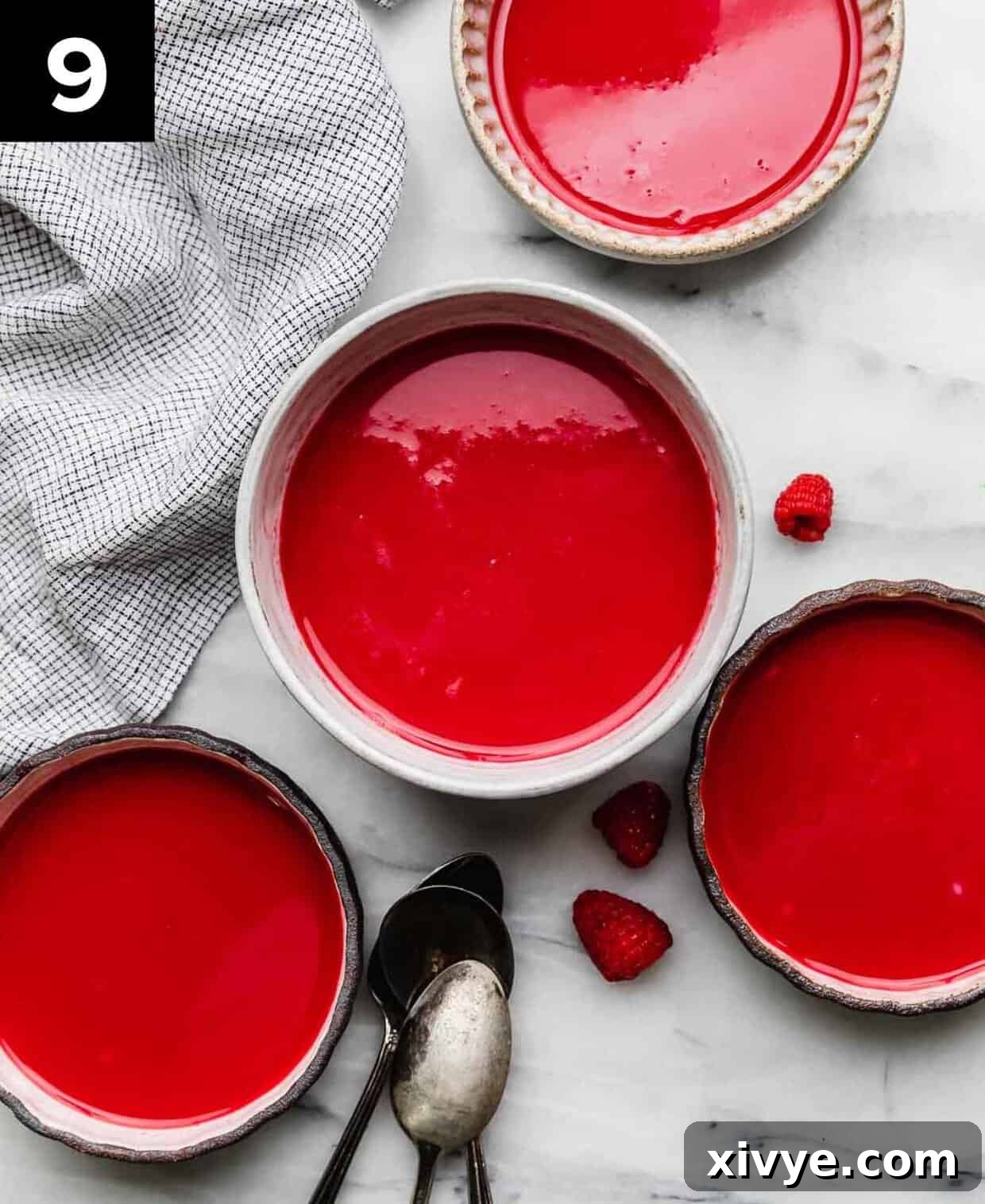 Four bowls filled with homemade Cold Raspberry Soup recipe on a white marble surface, garnished with fresh raspberries and mint.
