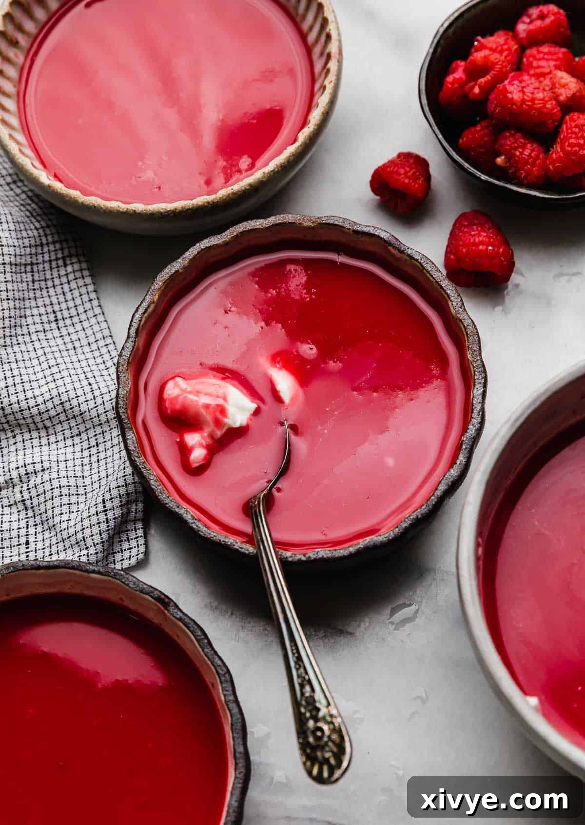 Whipped cream topped raspberry soup in a glass rimmed bowl with a spoon scooping out the whipped topping, on a light background.