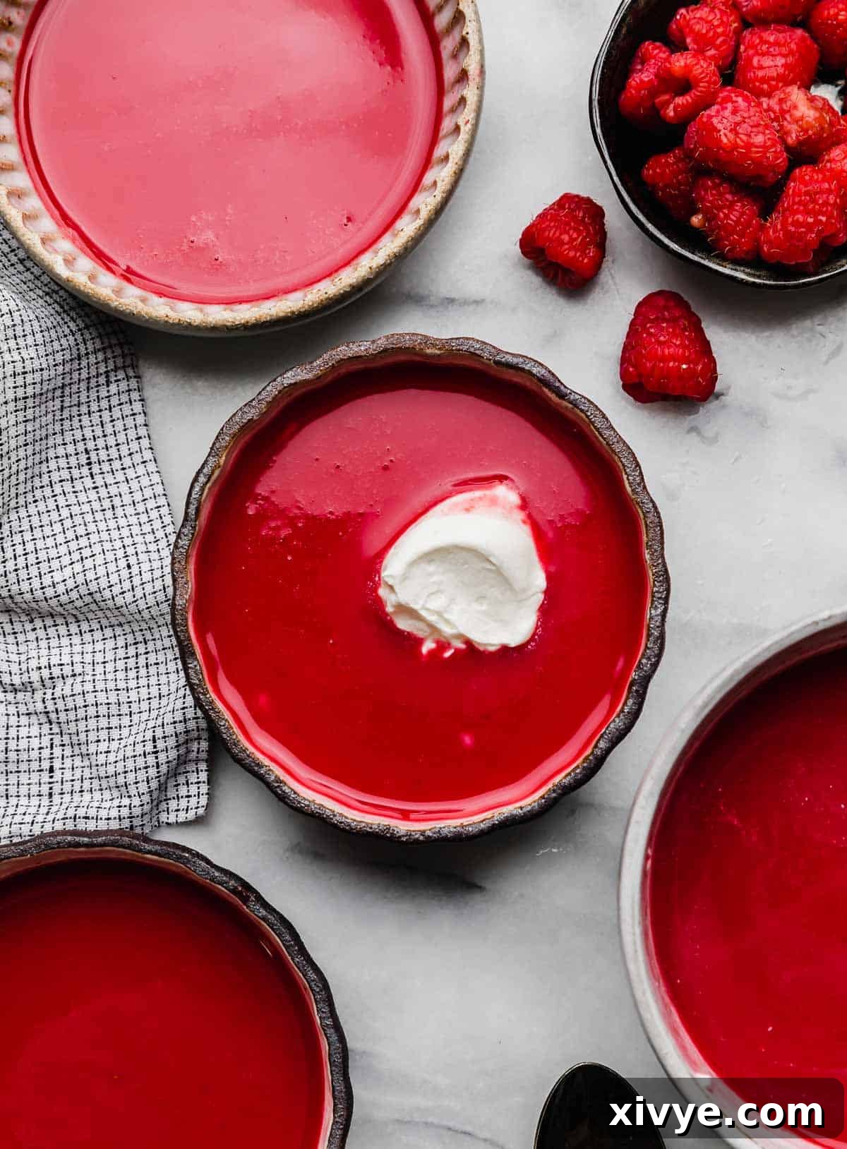 A dollop of whipped cream on top of a chilled raspberry soup in a glass bowl, with fresh raspberries on a white background.
