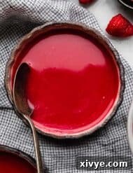 Cold Raspberry Soup in a black bowl with a spoon in the bowl and fresh raspberries near the bowl.