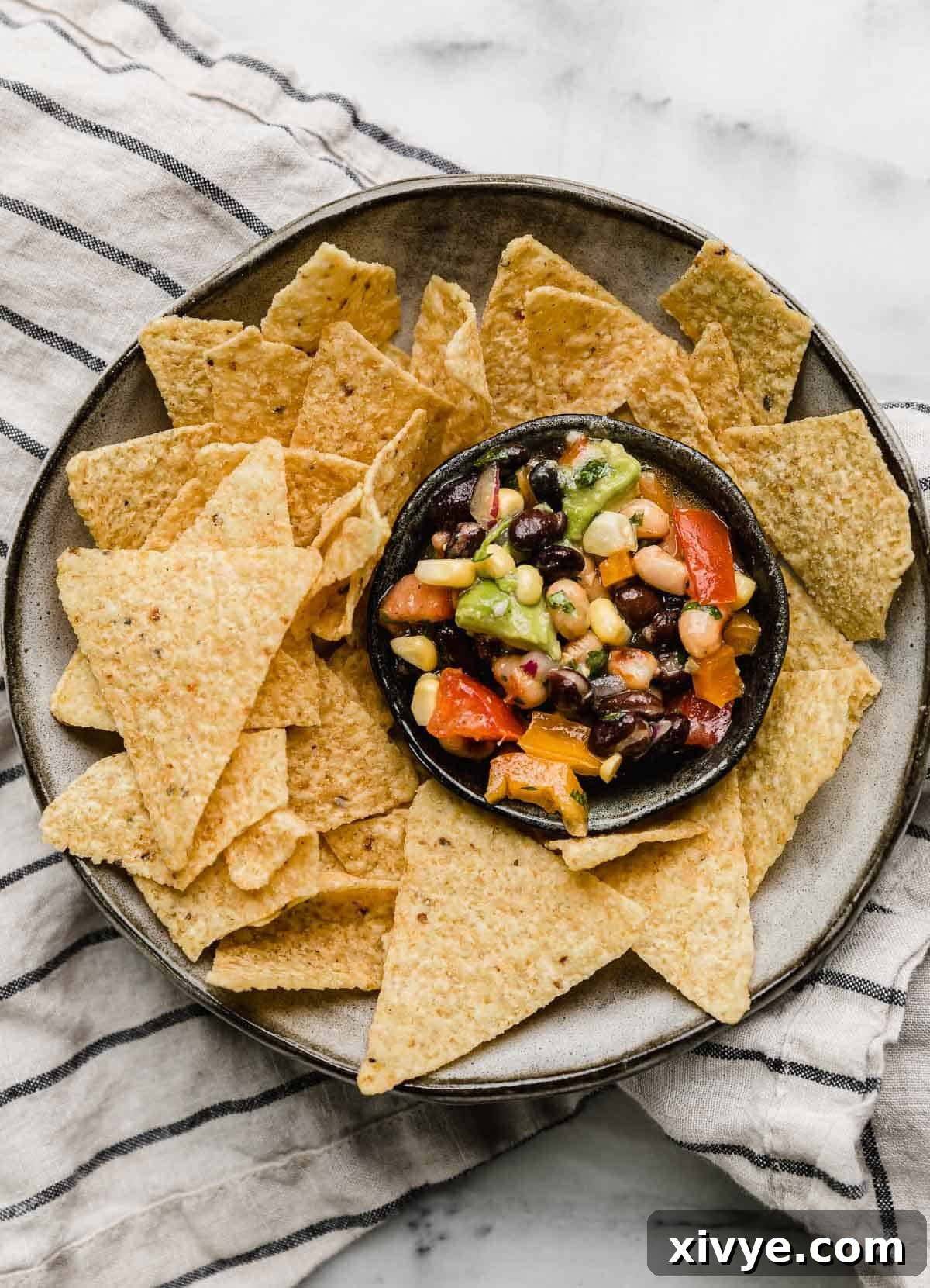 Vibrant Tex Mex Fiesta Salad 5 Overhead photo of Texas Caviar in a small black bowl that's on a gray plate surrounded by triangle tortilla chips.