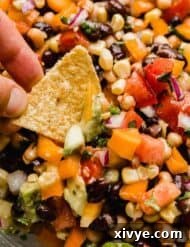 Vibrant Tex Mex Fiesta Salad 7 Texas caviar (diced tomatoes, peppers, beans, cilantro, and onion) in a glass bowl with a hand dipping a tortilla chip into the cowboy caviar recipe.