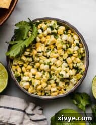 Overhead photo of corn salsa made with raw corn in a black bowl on a white background with fresh limes surrounding the bowl.